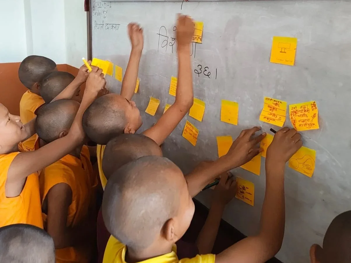 Group of young children in yellow uniforms working together, placing yellow sticky notes on a classroom whiteboard.