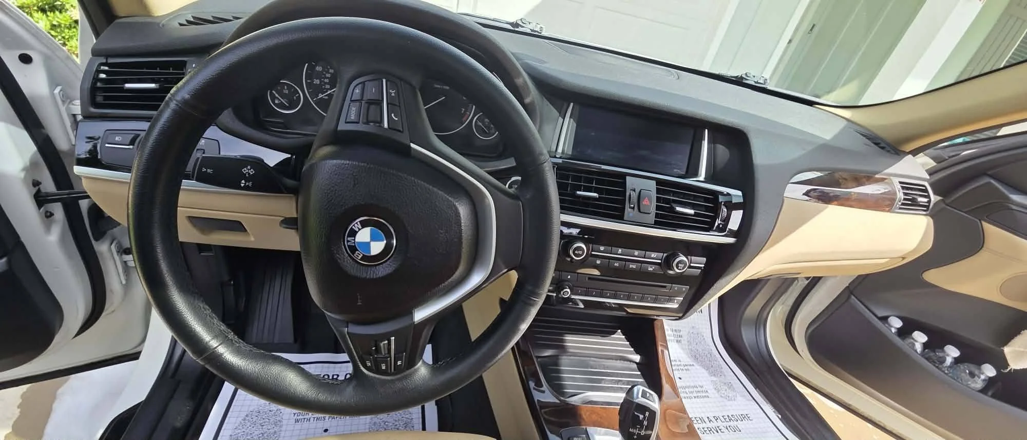 Interior of a BMW car showing the steering wheel, dashboard, and center console with controls and a large display screen.