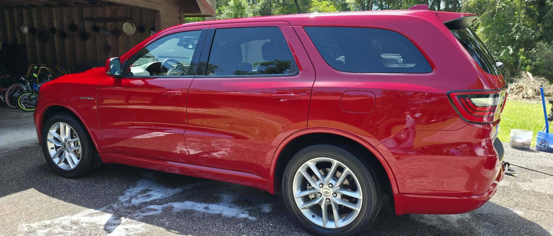 Red SUV parked in a Wakulla County driveway next to a wooden shed, with bicycles and gardening tools in the background and some soap suds or water on the ground.