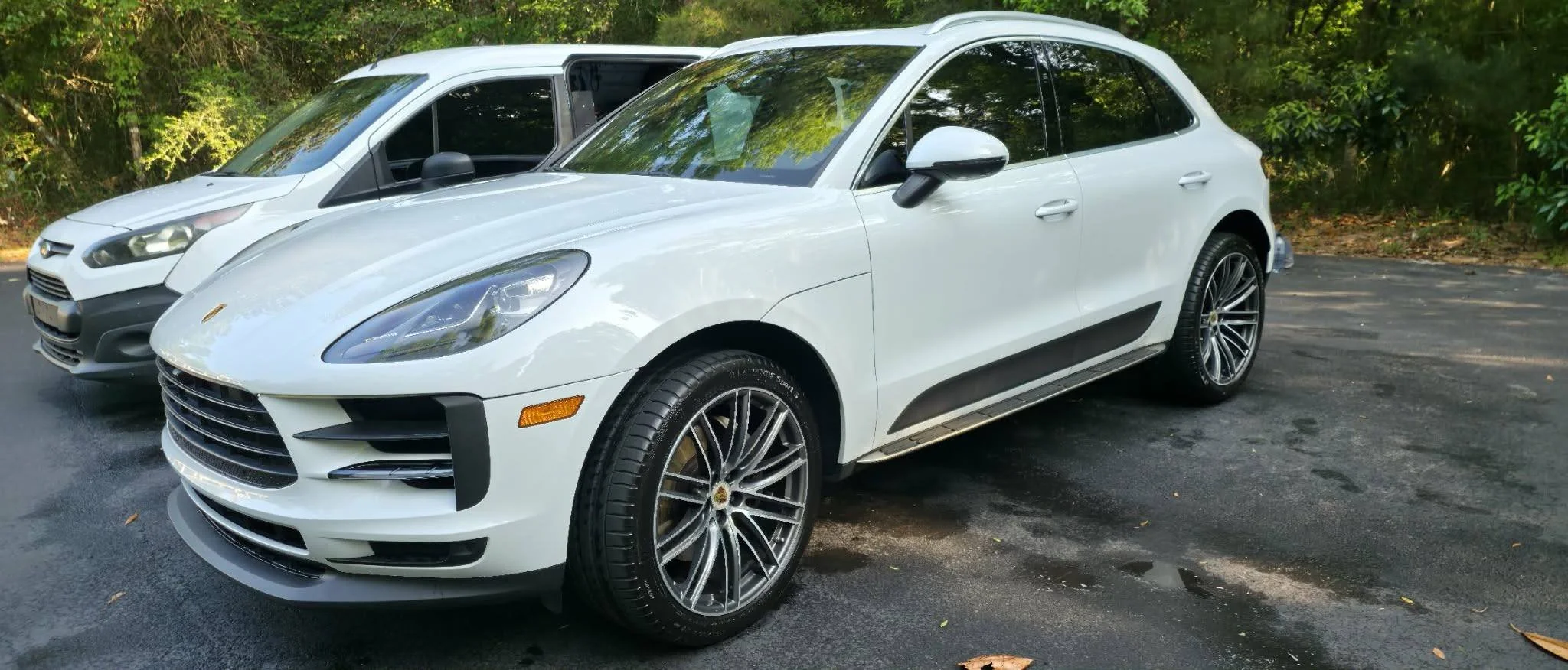 White luxury SUV parked on asphalt with green trees in background.