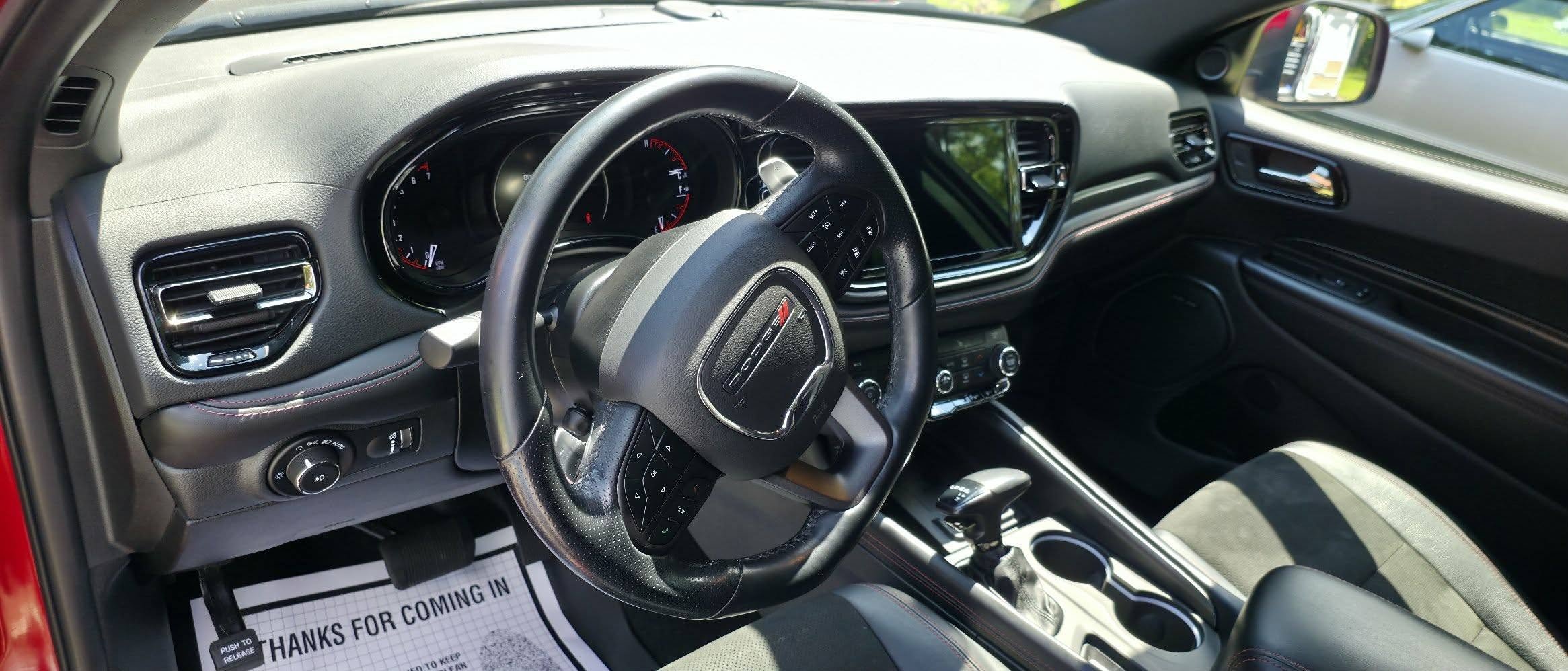 Interior view of a vehicle dashboard and steering wheel, with an automatic gear shift, air vents, and a touchscreen display.