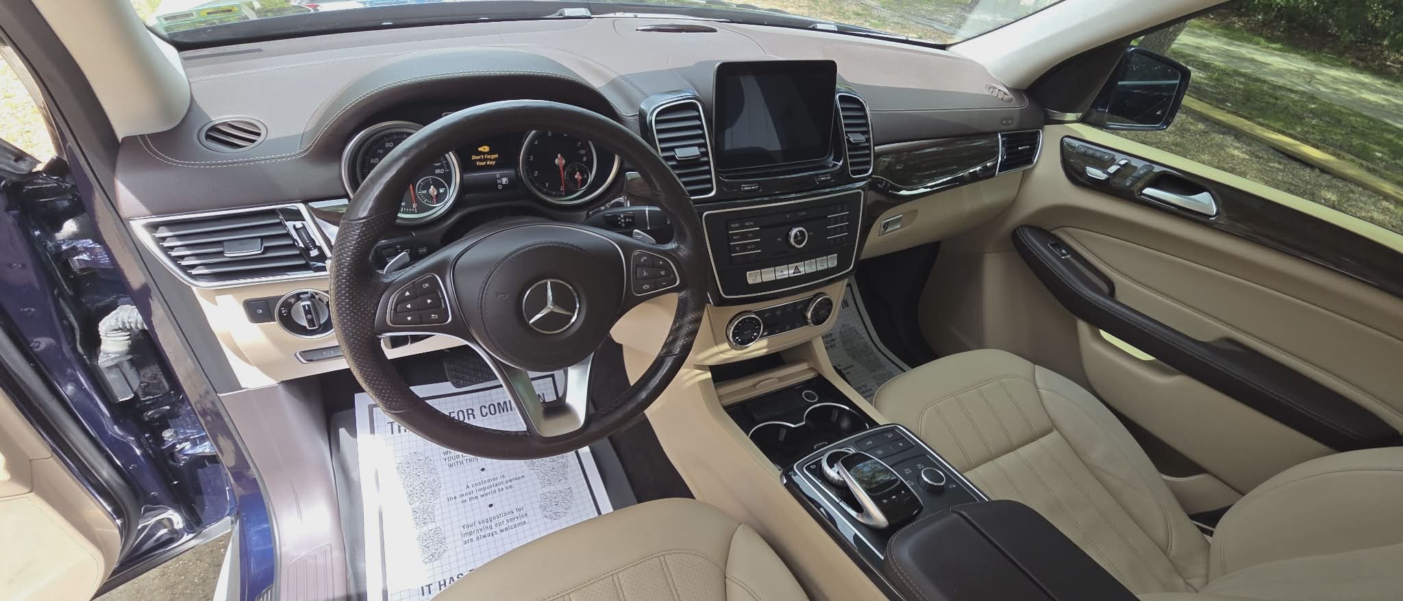 Interior of a luxury Mercedes-Benz vehicle, showing the steering wheel, dashboard, center console, and beige leather seats.