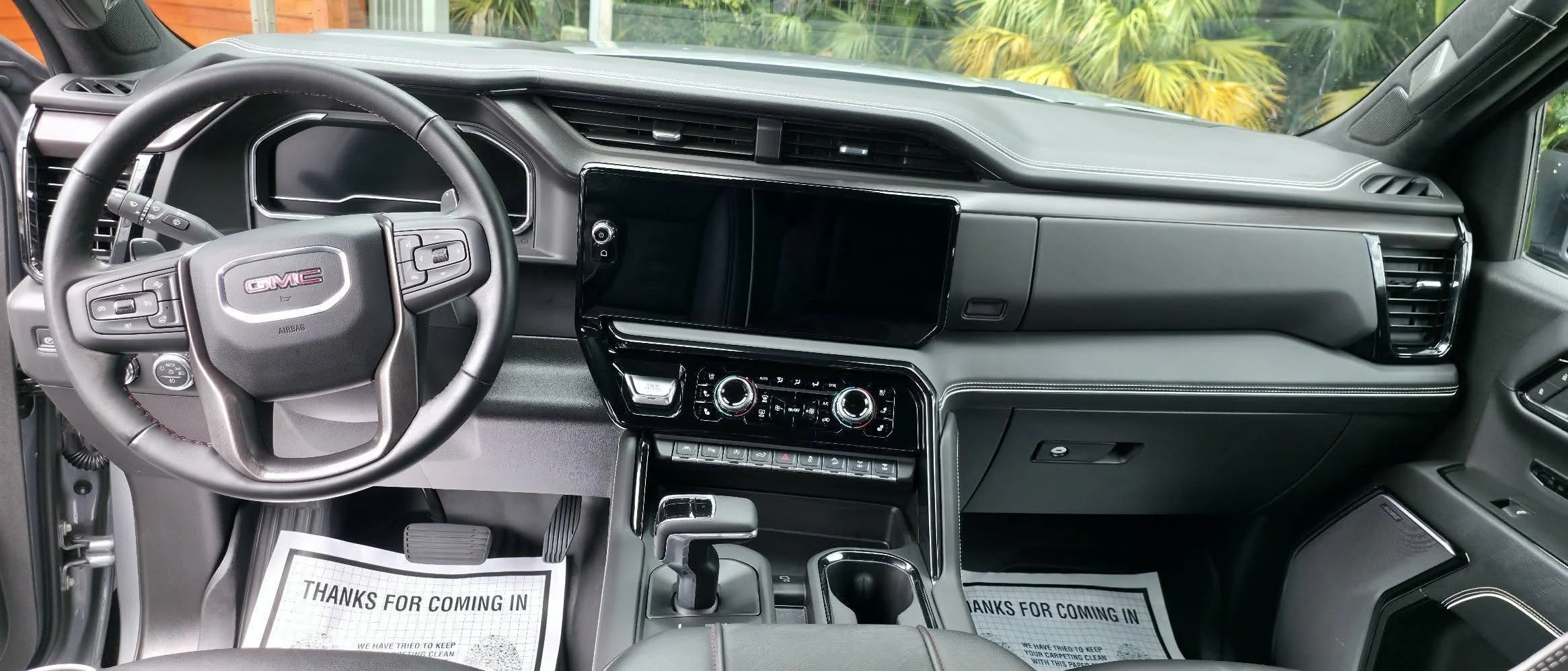 Interior of a GMC vehicle dashboard with steering wheel, digital display, and center console, looking from the driver's side.