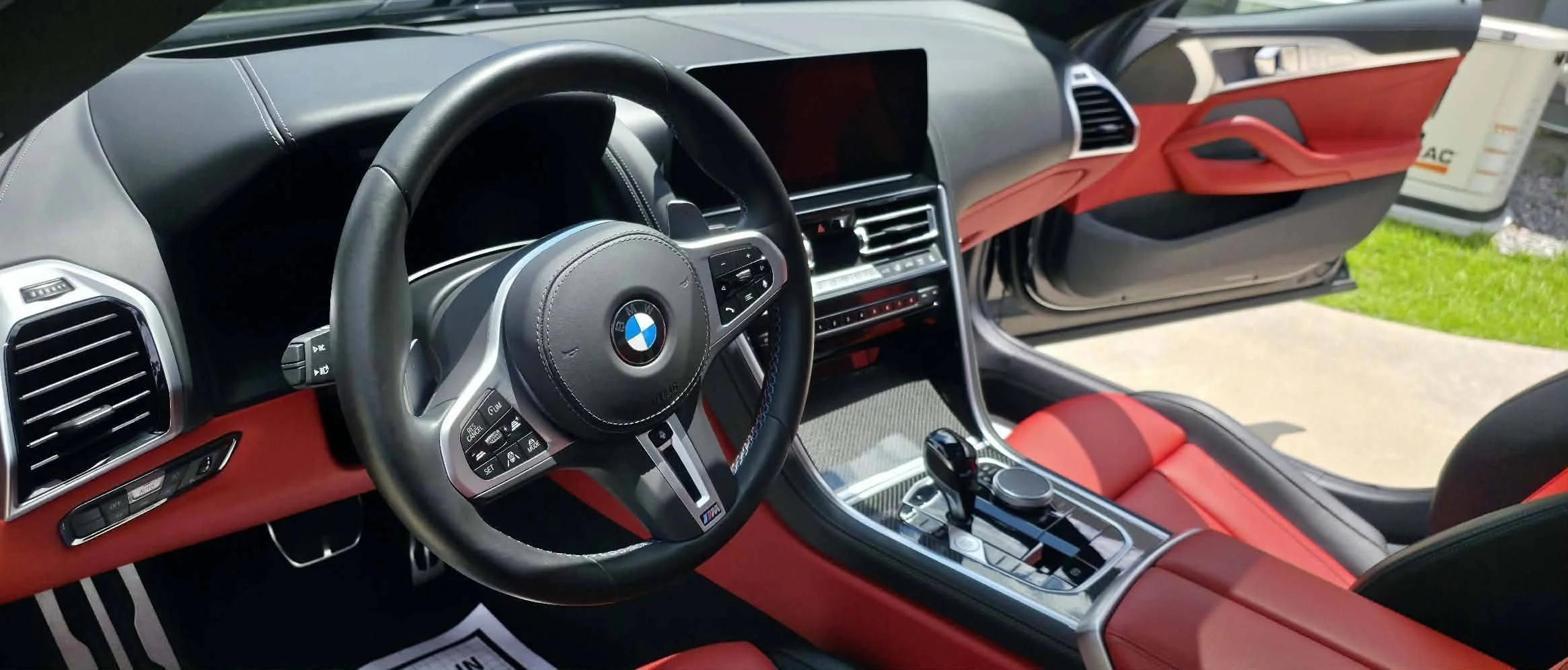 The interior of a BMW car with a black and red color scheme, featuring a steering wheel with BMW logo, digital display, and central console with controls.