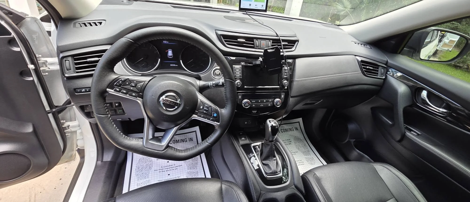 Interior of a Nissan vehicle showing the steering wheel, dashboard, center console with gear shifter, and a mounted smartphone.