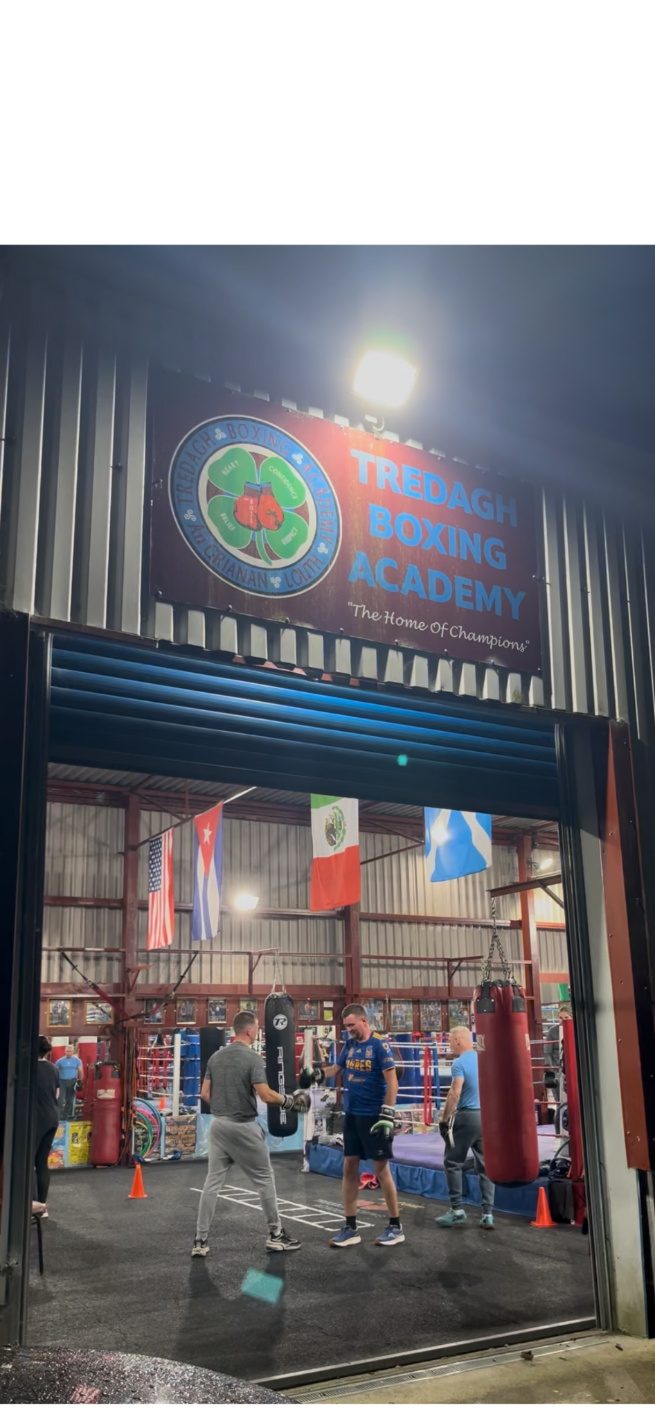 Indoor boxing gym with people training, punching bags, colorful flags, and boxing posters.