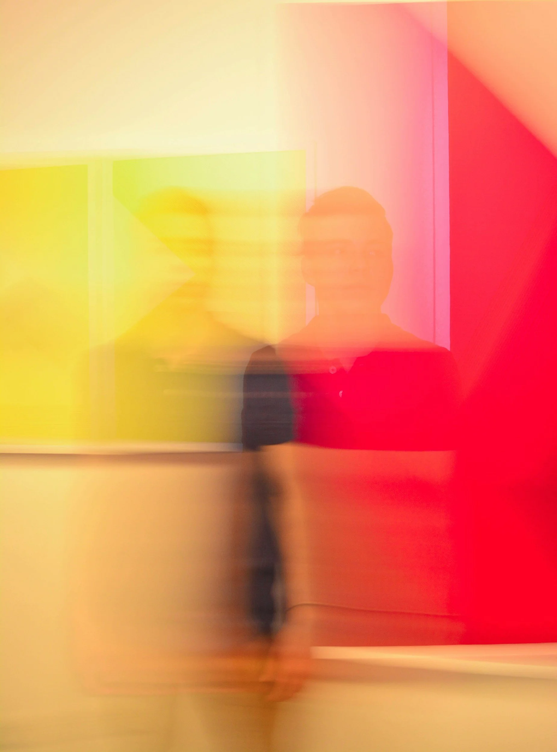 A person standing in front of a colorful background with yellow and red sections, with motion blur creating a layered, abstract effect.