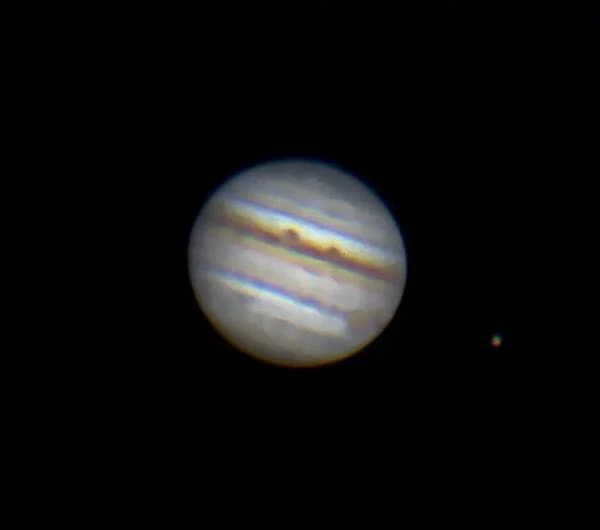 A view of Jupiter with its colorful bands and the small moon Io visible nearby, against a black space background.