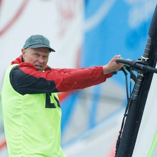 A man in a red jacket, black cap, and neon yellow vest operating sailing equipment.