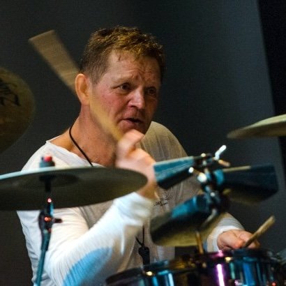 A man playing the drums, captured in a close-up during a performance or rehearsal.