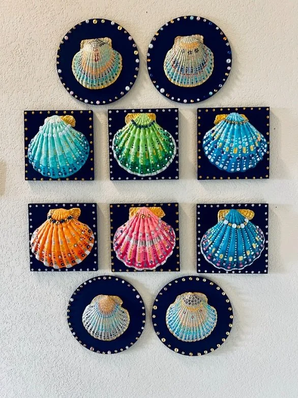 Wall display of nine colorful seashell paintings arranged in a grid with three rows and three columns, each with a black background and decorative border.
