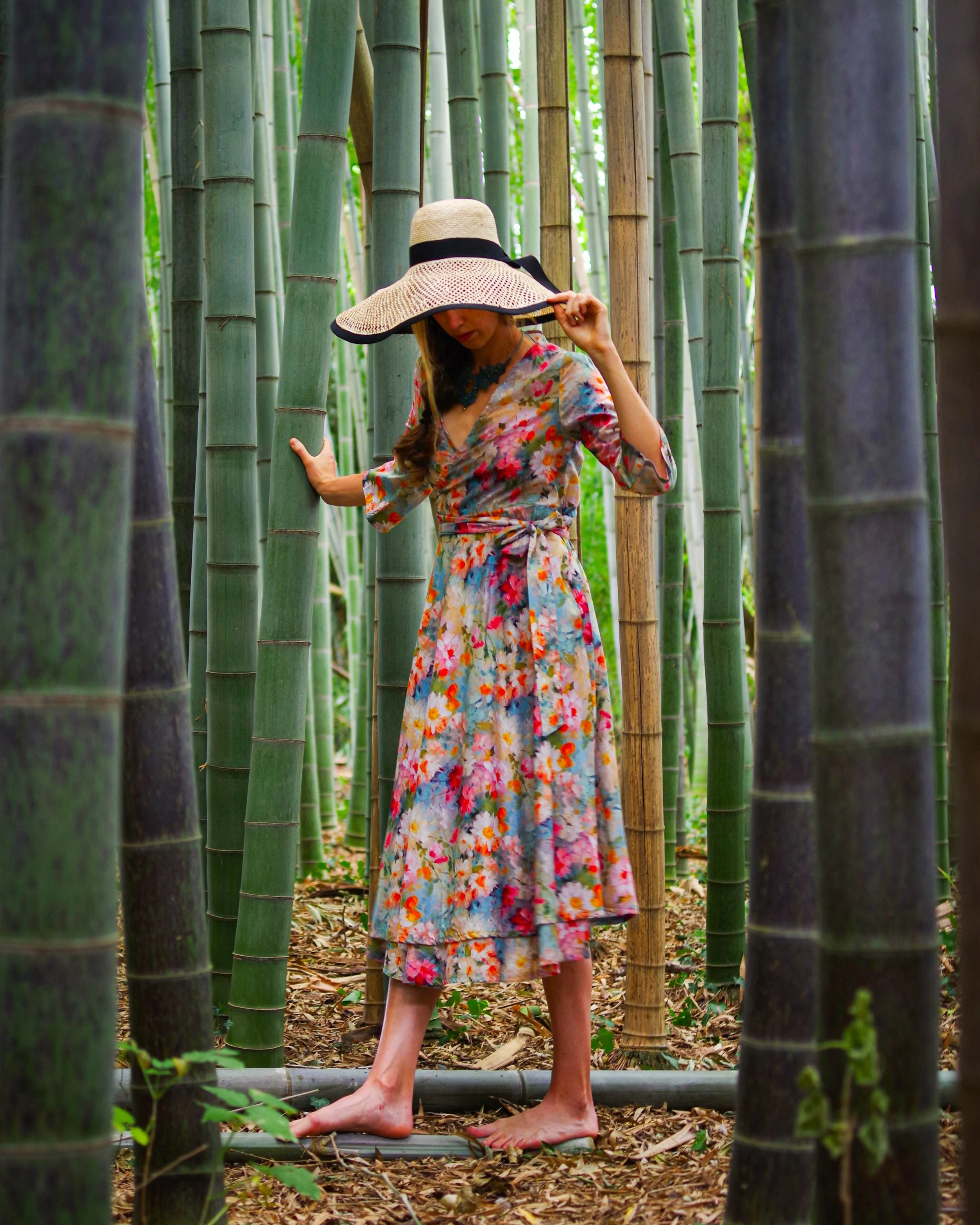 Una donna con abito floreale e cappello di paglia in un campo di bambù.