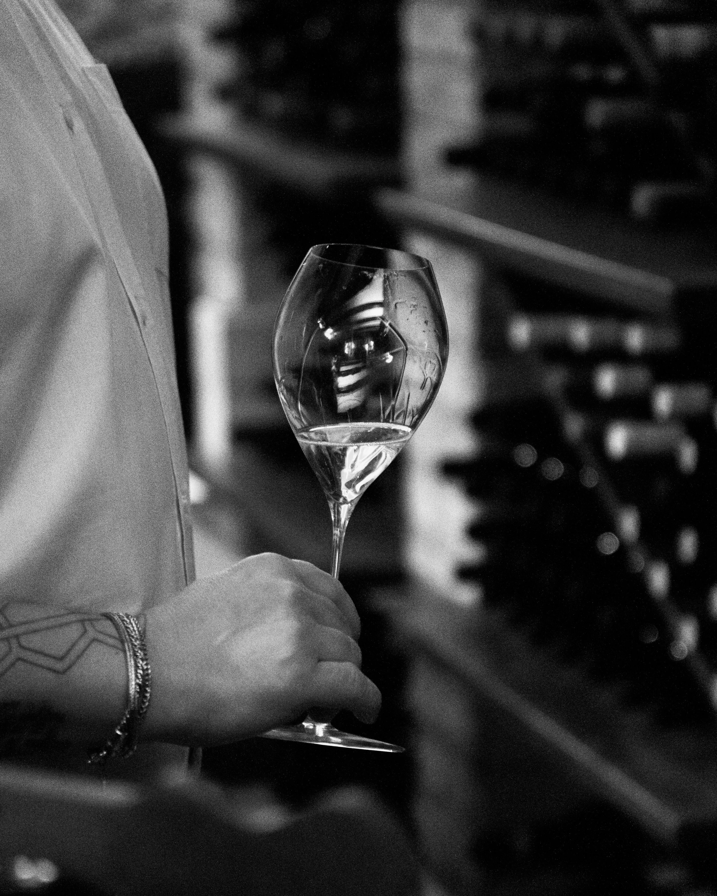 sommelier che tiene in mano un bicchiere di vino all'interno della cantina piena di bottiglie di vino