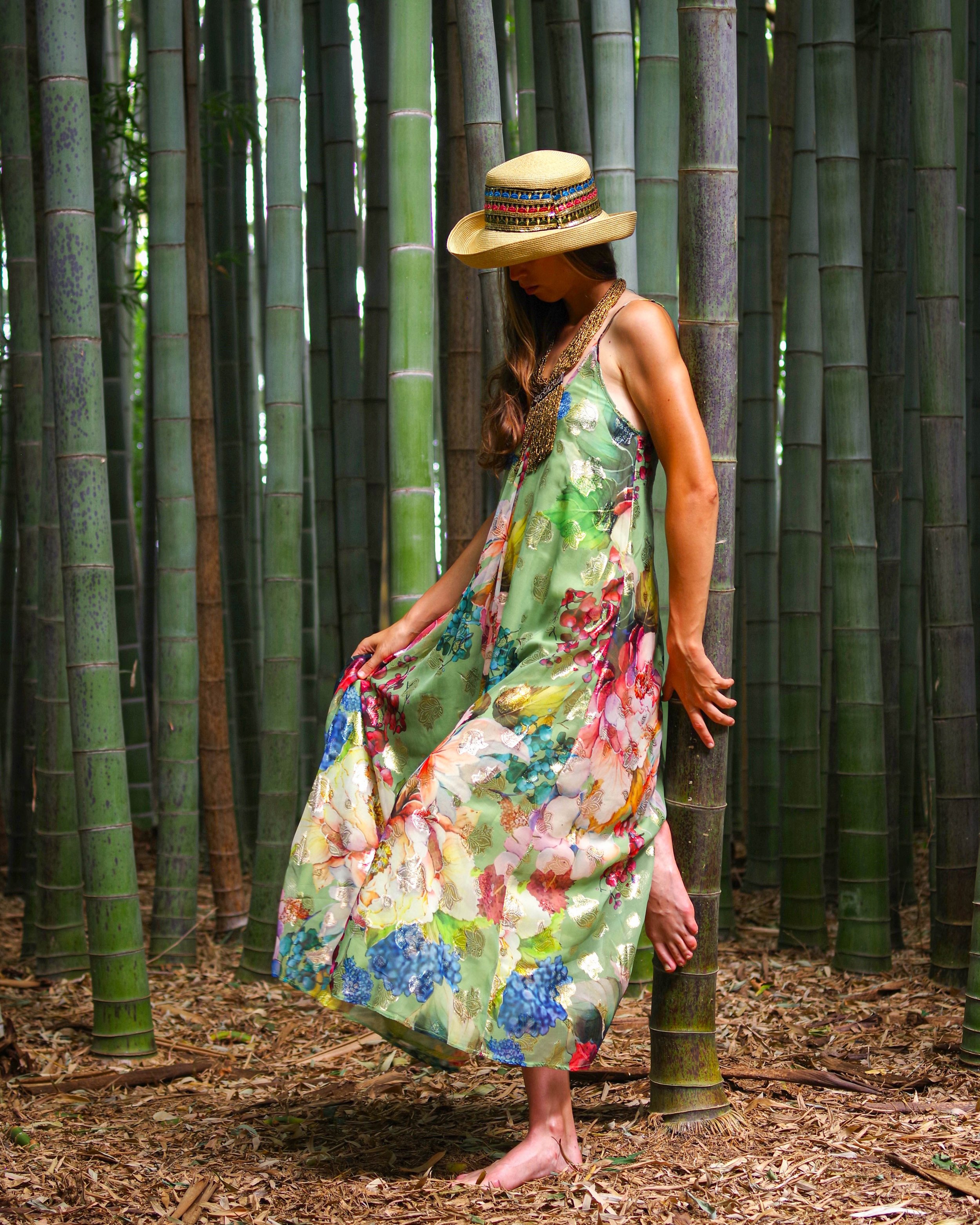 Una donna indossa un abito floreale lungo e un cappello di paglia mentre si trova in una foresta di bambù.