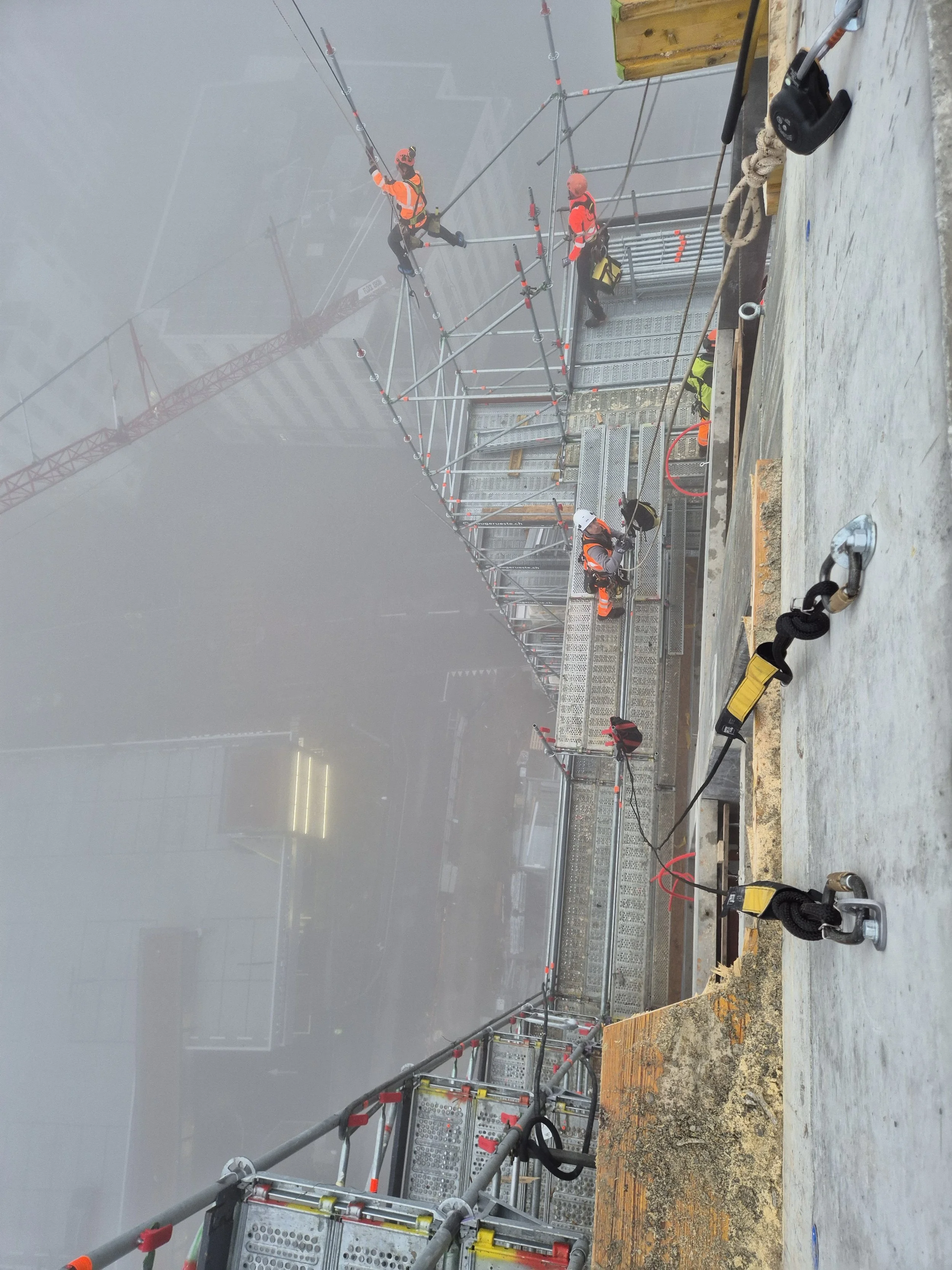Bauarbeiter auf einer Baustelle, die auf einer hohen Gerüstplattform Arbeiten ausführen, umgeben von Sicherheitsausrüstung
