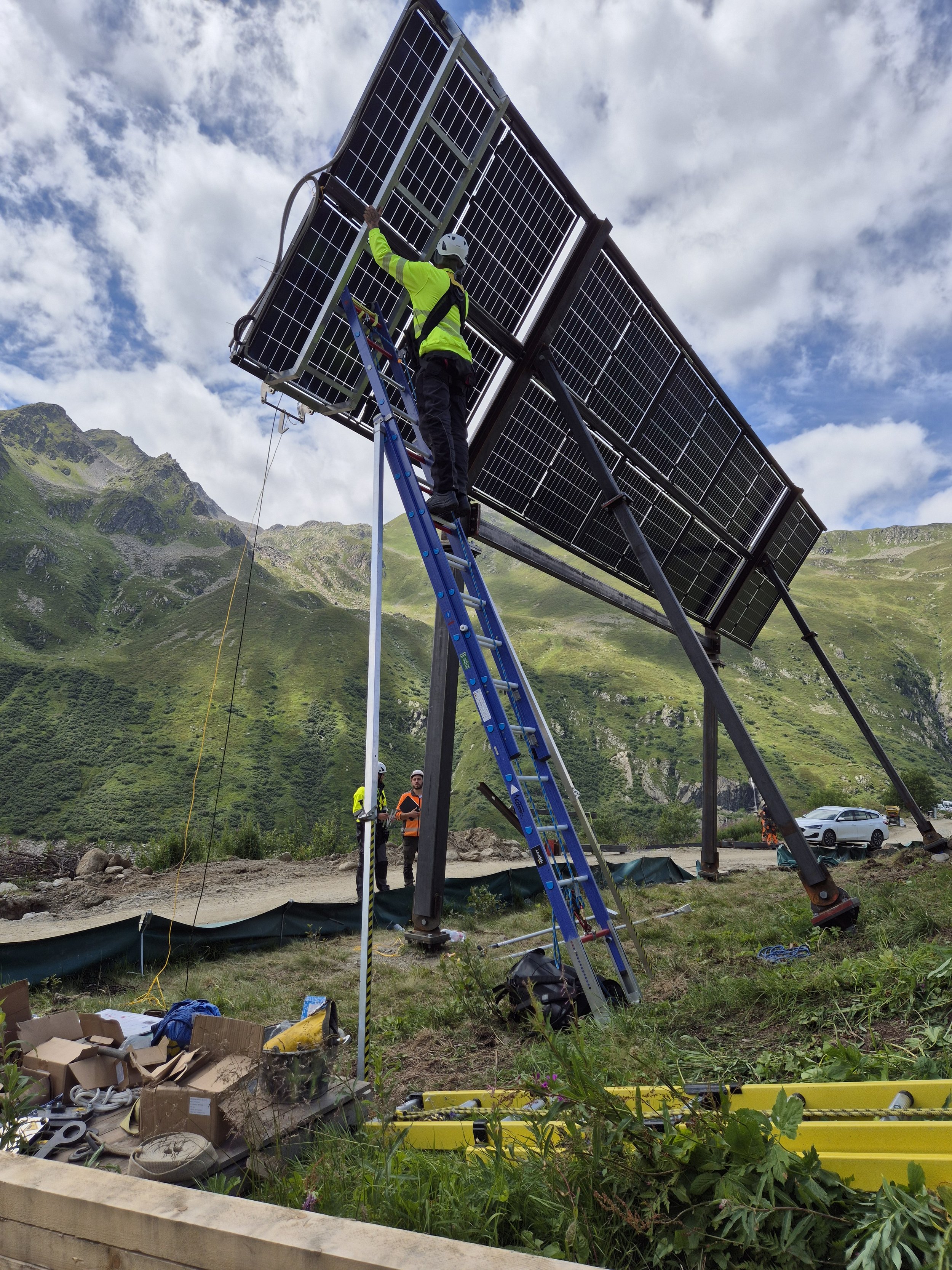 Ein Indstriekletterer in Sicherheitskleidung arbeitet an einer Solaranlage auf einem Gestell in einer bergigen Landschaft.