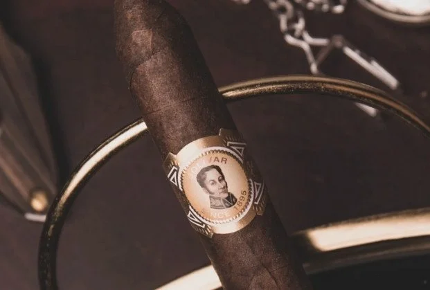 Close-up of a cigar resting on a metallic stand, with a band featuring a woman's portrait.