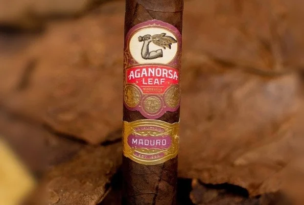 A close-up of a cigar with a colorful band that reads "Agnorsa Leaf" and "Maduro," featuring a stylized logo of a bird.