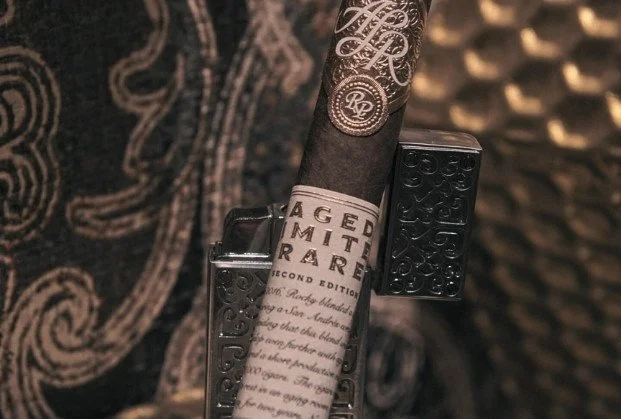 A Black & Mild cigar with decorative silver designs, a paper wrapper, and a black Zippo lighter attached to the side.