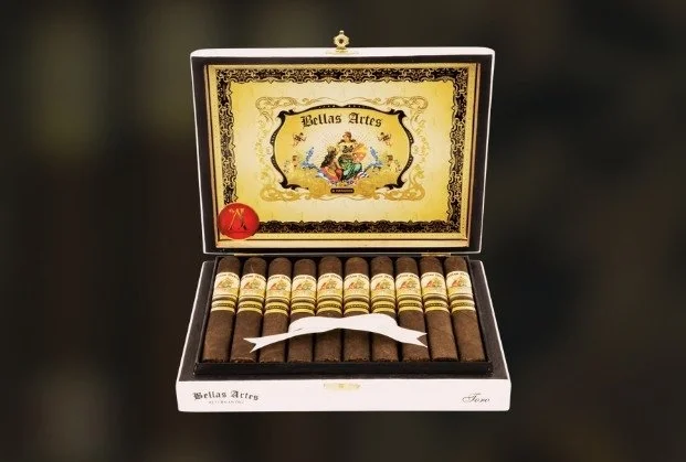 Open box of cigars with decorative label inside lid and a small red ball and a white band or ribbon in the box.