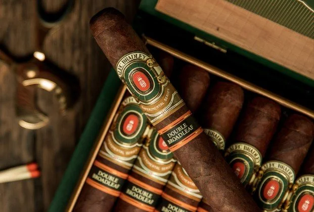 Open cigar box with cigars inside and a single cigar resting on top.