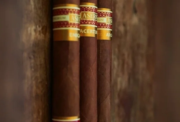 Close-up of three cigars with gold and red bands resting on a wooden surface.