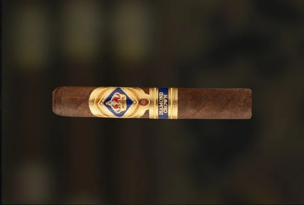 A lit cigar resting on a dark surface with a blurred dark background.