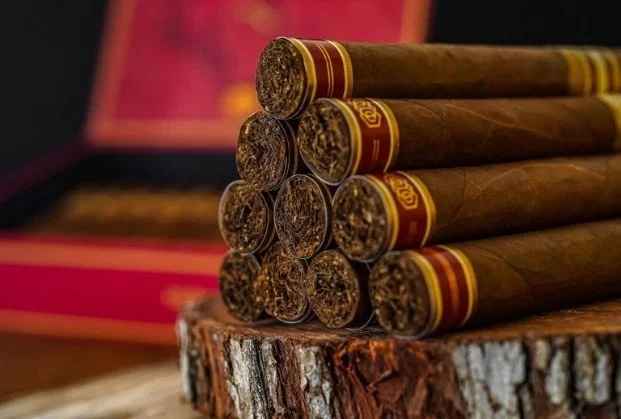 A stack of cigars resting on a wooden surface with a blurred background.