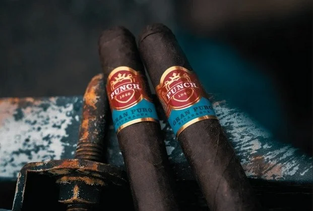 Two cigars with Punch branding and a burnt-out cigar laying on a surface.