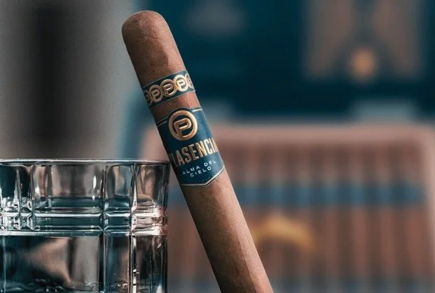 A cigar with a decorative band resting against a glass of water.