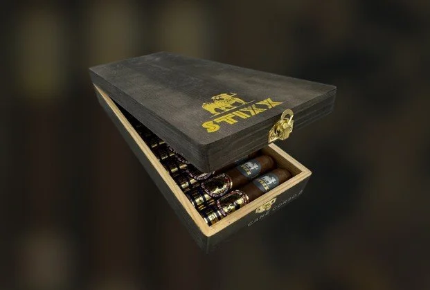 A black wooden box with a gold latch, opened to reveal cigars inside, with the word 'STIG' and a logo printed on the top.