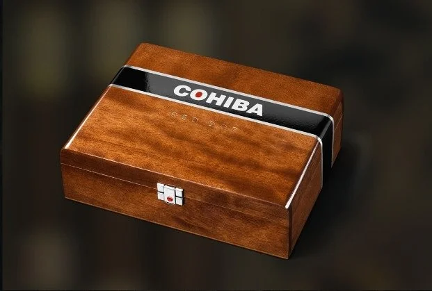 A wooden cigar humidor box with a black and white band that reads 'COHIBA' on the lid.