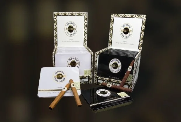 Open boxes of Ashton cigars with cigars placed on a small table and a black metal box nearby.