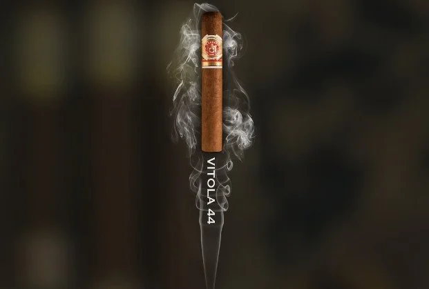 Cigar with smoke rising from it, labeled 'VITO.LA 44', with a blurred dark background.