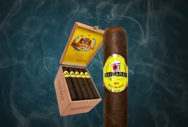 A large cigar on a dark, smoky background with a box of smaller cigars open beside it.