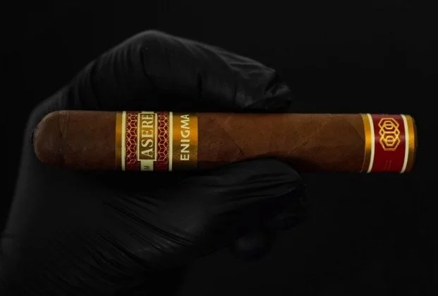A hand wearing a black glove holding a lit cigar with a red and yellow band against a black background.