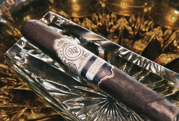 A cigar resting on a decorative glass ashtray with a gold background.