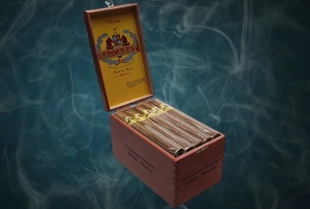 Open cigar box containing cigars with smoke rising in the background.