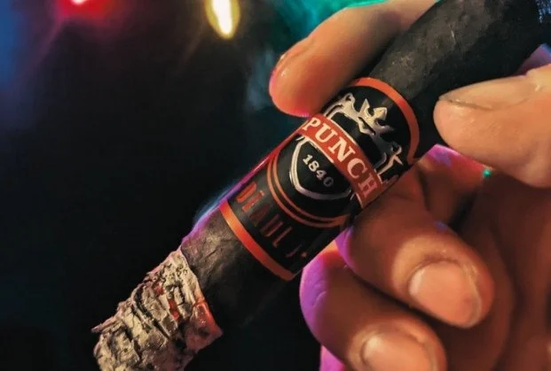 Close-up of a person holding a lit cigar with a red and black band.