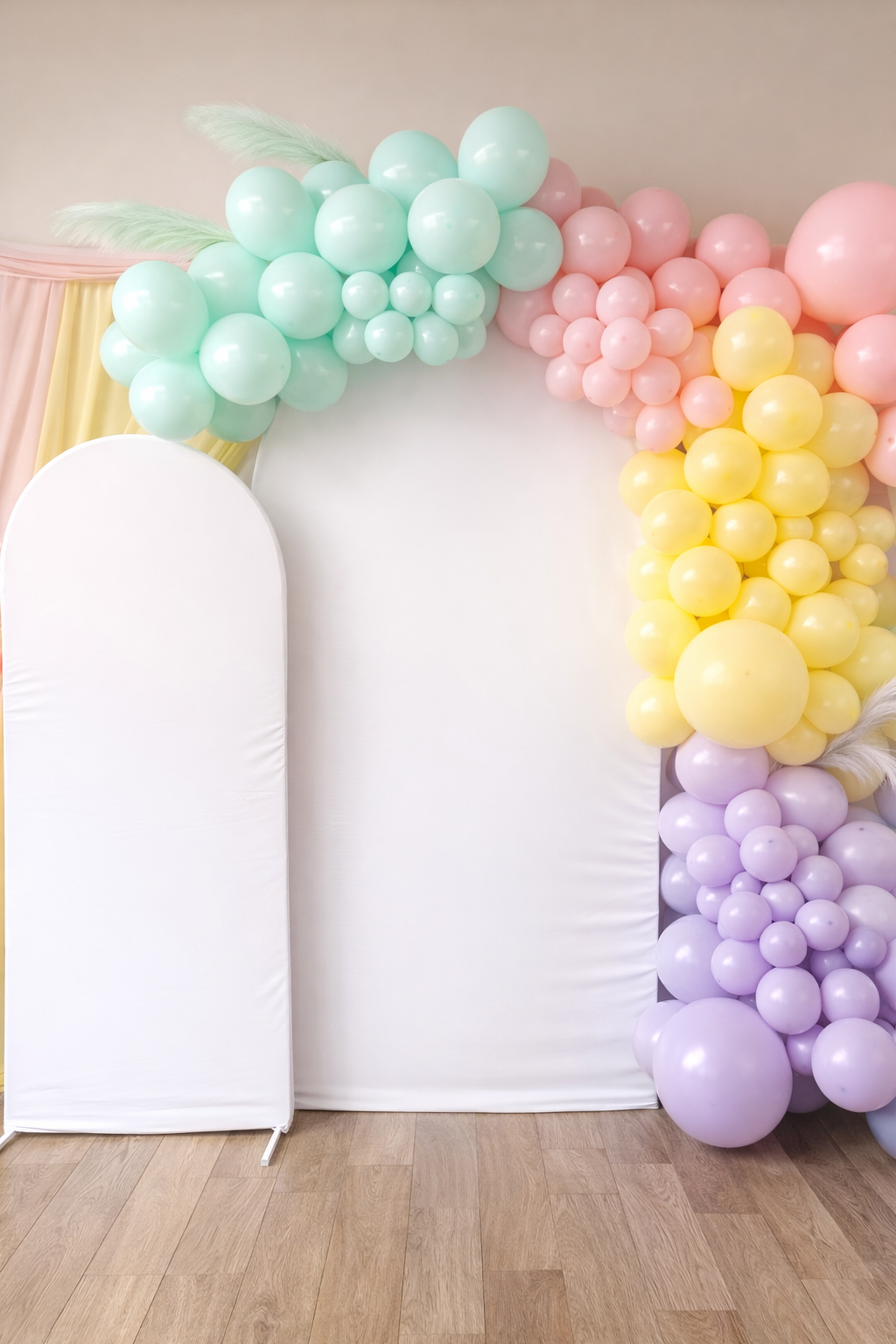 Colorful balloon arch with pastel green, pink, yellow, and purple balloons decorating a white backdrop with a whiteboard, on a wooden floor.