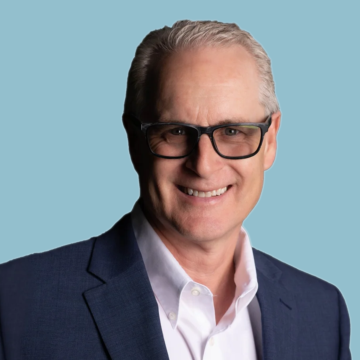 Portrait of a middle-aged man with short, light-colored hair, wearing a light blue patterned dress shirt, standing against a plain white background.