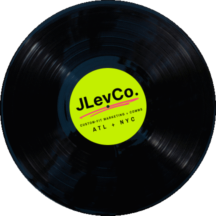 A black vinyl record with a bright yellow label in the center that reads "JLeVCO. Custom Fit Marketing + Comms ATL + NYC".