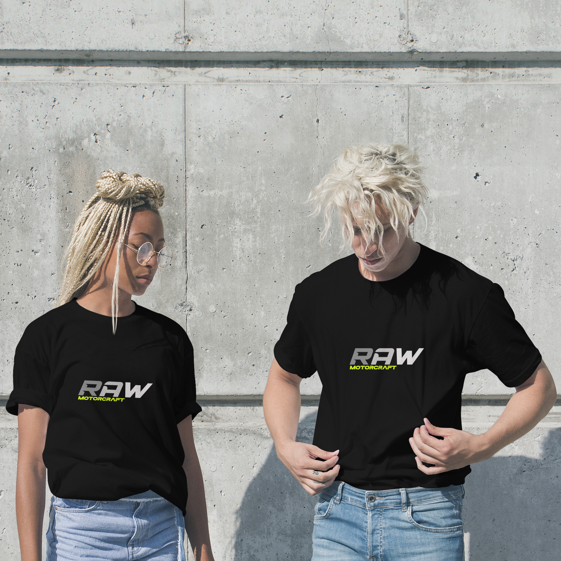 Two young people standing against a concrete wall, both wearing black t-shirts with the logo 'RAW MOTORCRAFT'.