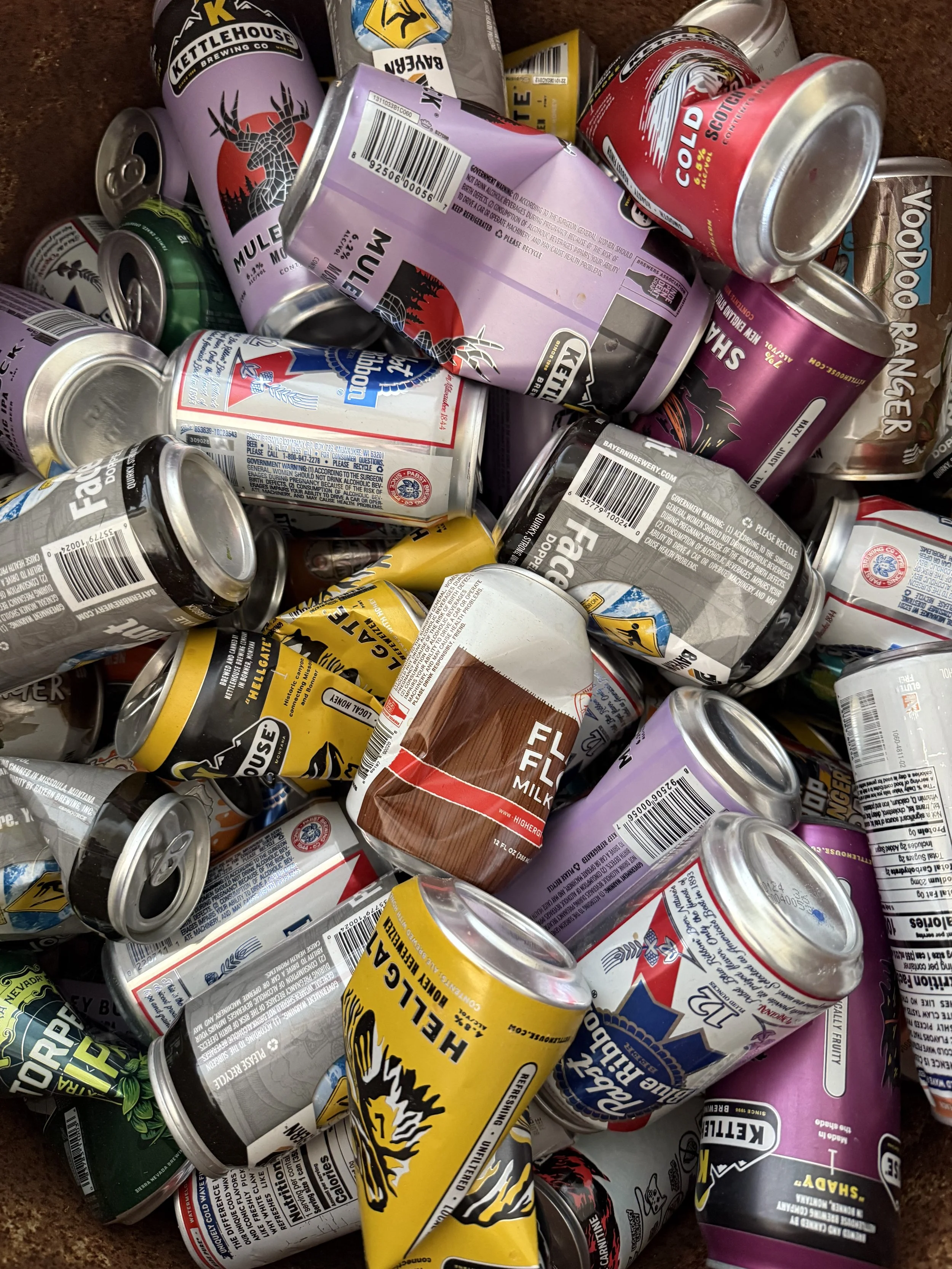A pile of empty beverage cans, including beer, soda, and energy drinks, some with recognizable brand labels.