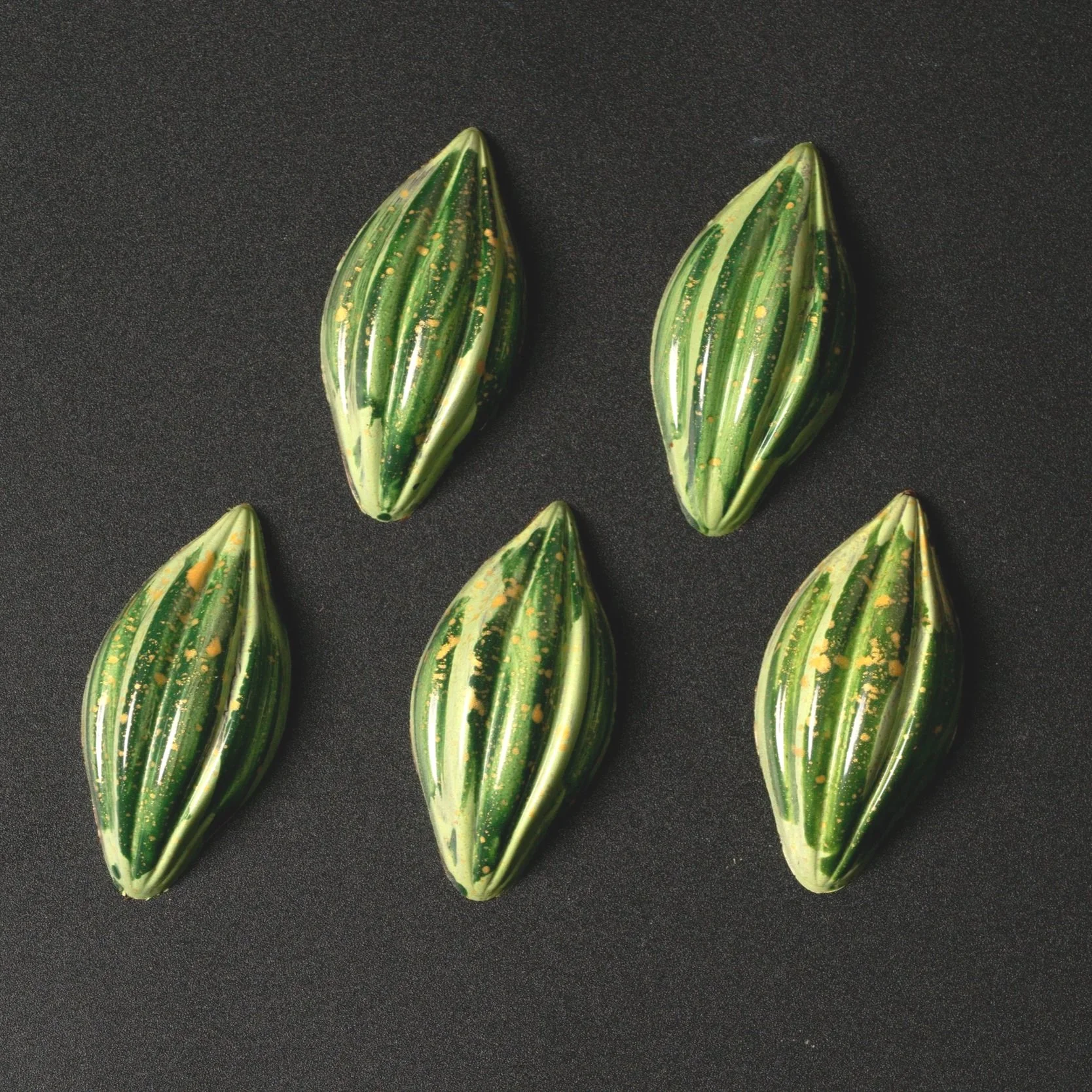 Five striped, green and yellow chocolates on a black background.