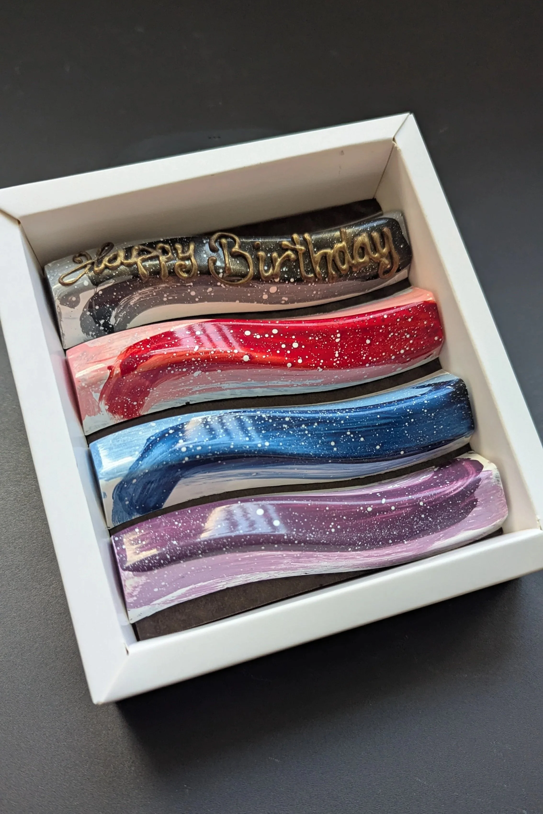 A box of five colorful, glittery, galaxy-themed chocolate bars, one with a "Happy Birthday" message.