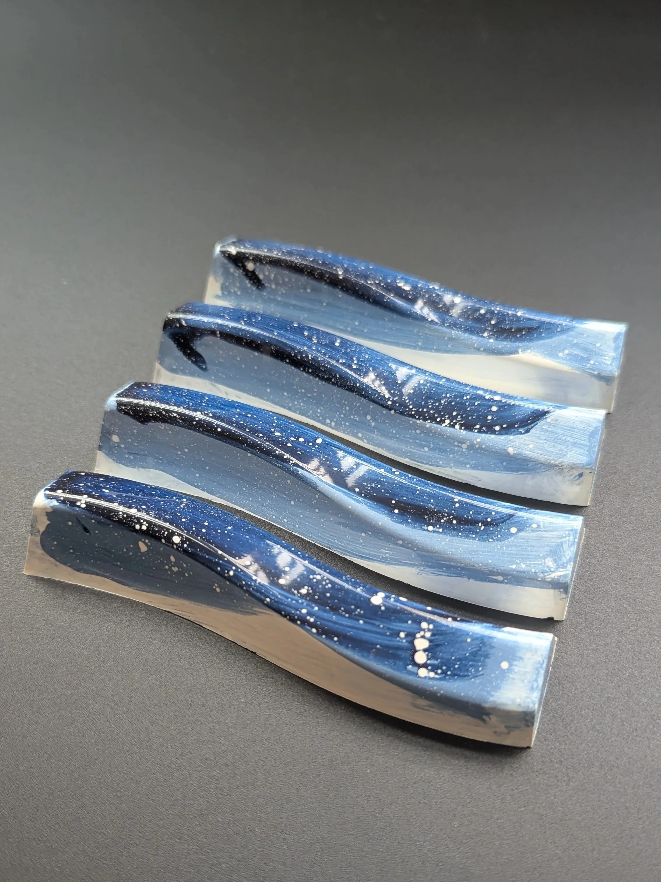 Four polished, blue and white marble-like chocolate bars with splatter patterns, arranged diagonally on a dark surface.