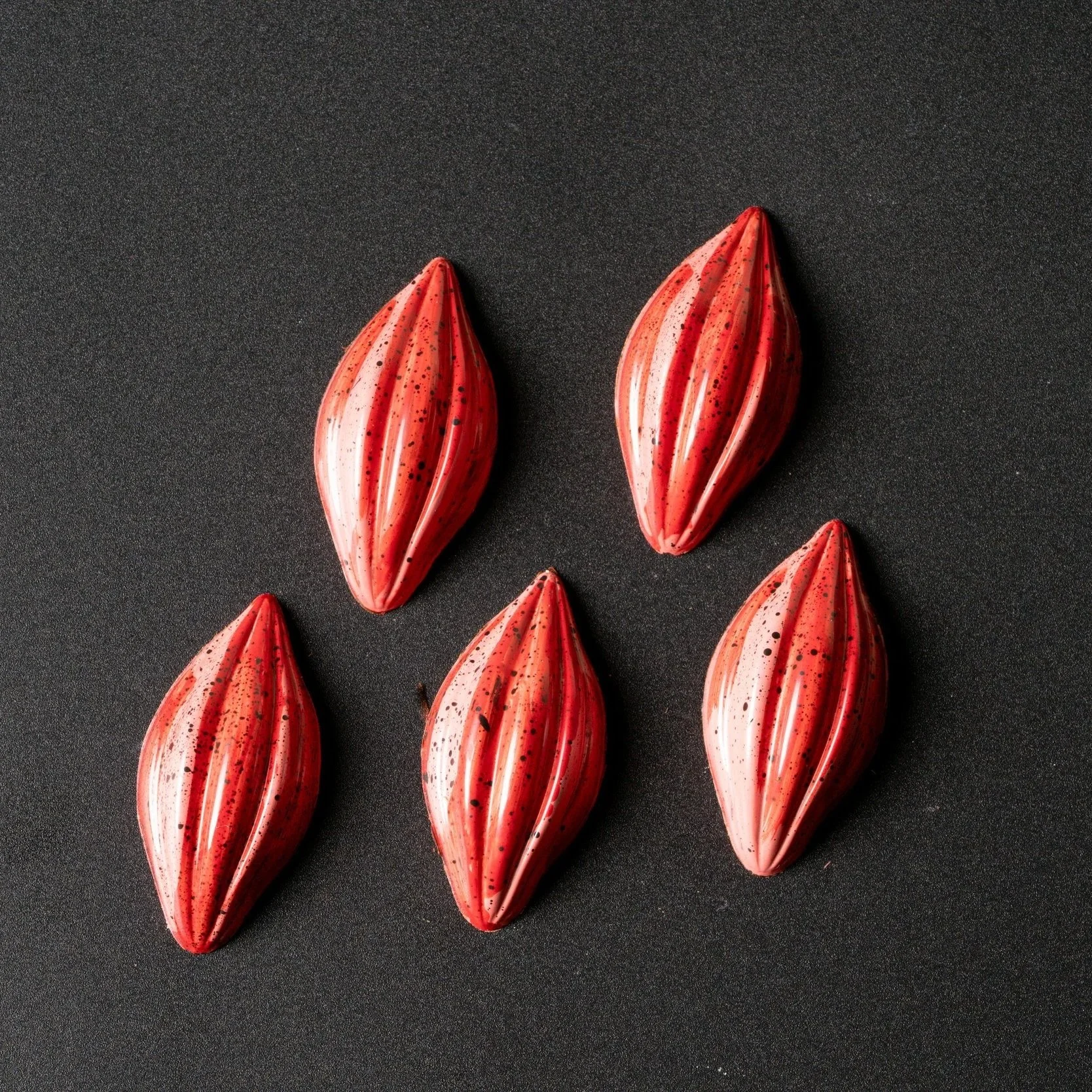 Five teardrop-shaped, red and white striped candies with black speckles on a black background.