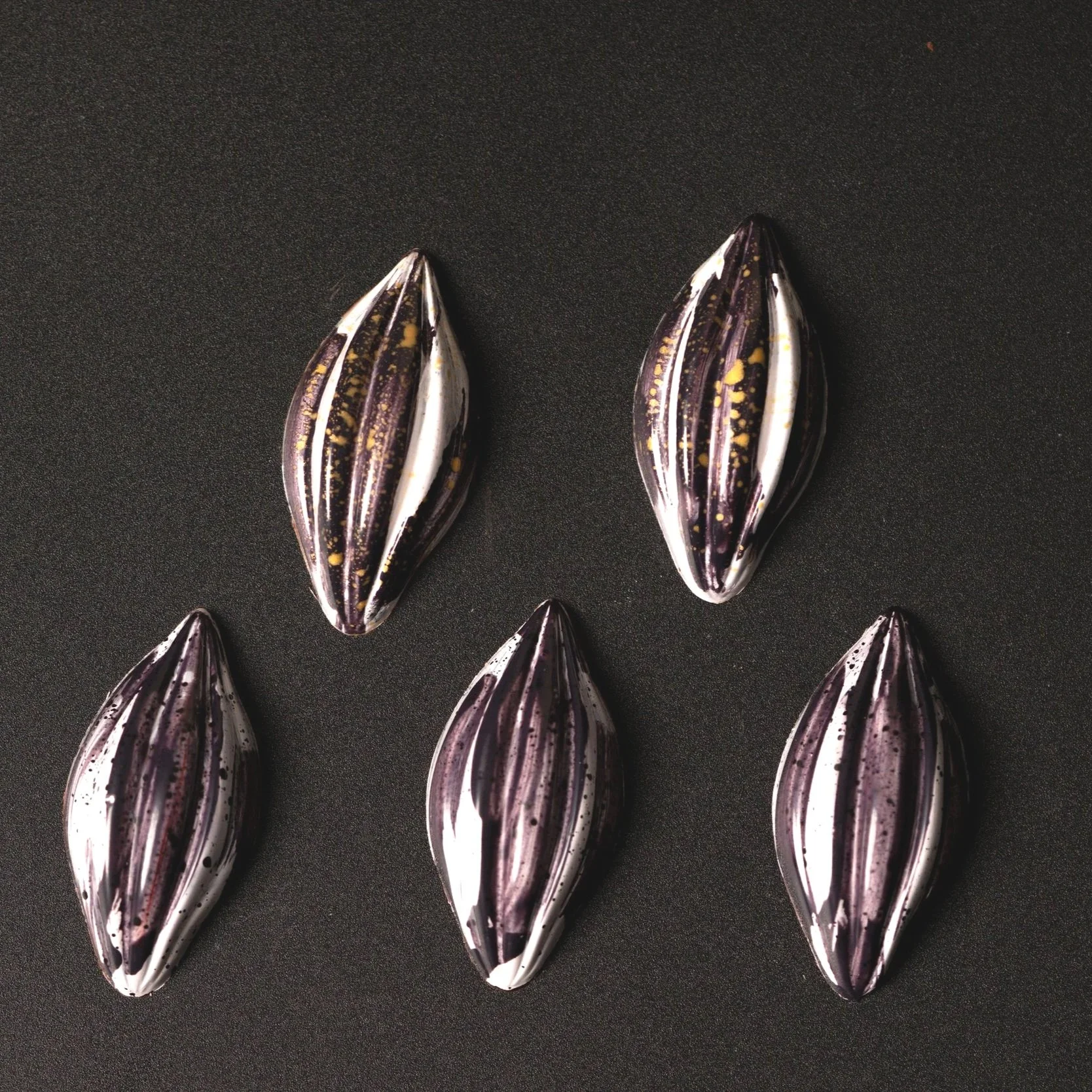 Five zebra-patterned elongated chocolates with black, white, purple, and gold colors on a black background.