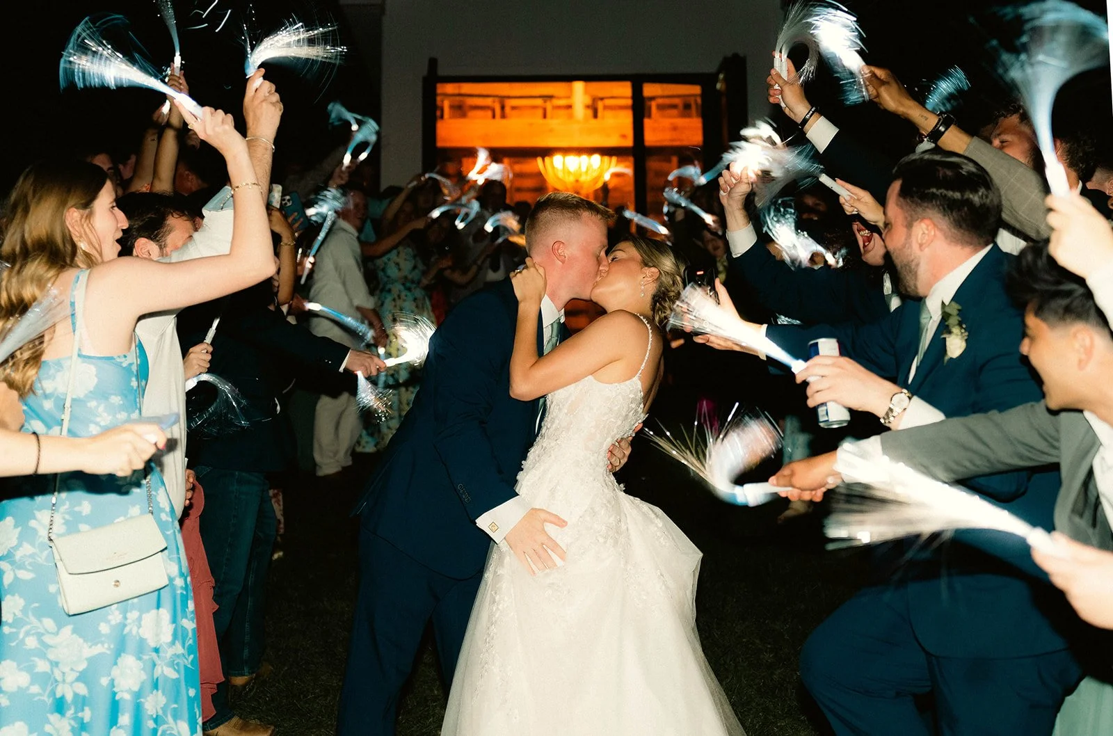A newlywed couple sharing a kiss during their wedding reception surrounded by guests holding sparklers.
